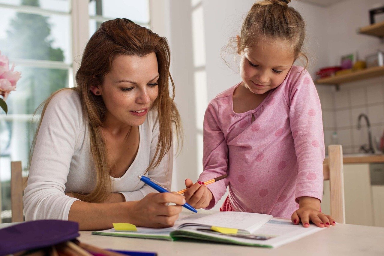 mother and daughter happily work on homework at kitchen table; remote learning concept