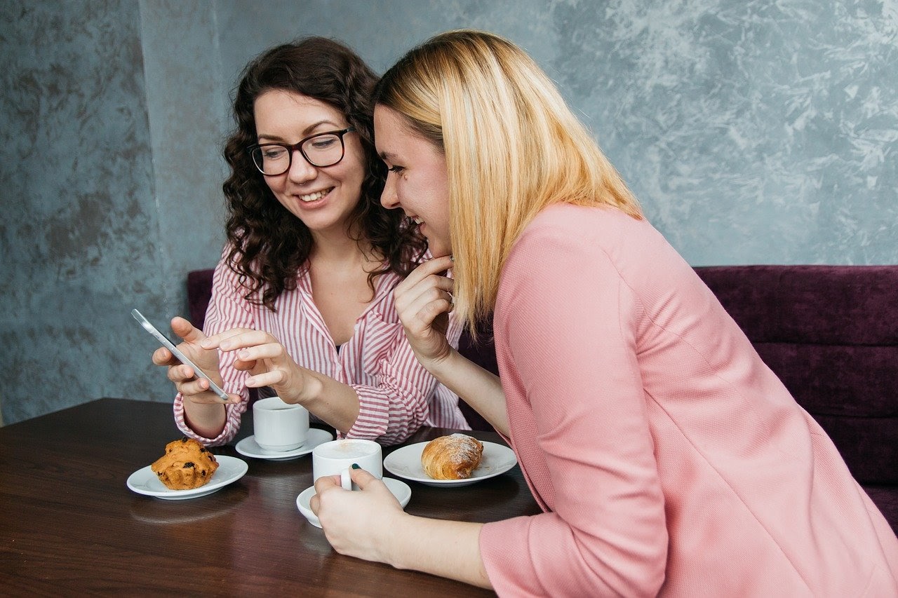 two women at cafe looking at smart phone; teacher burnout concept