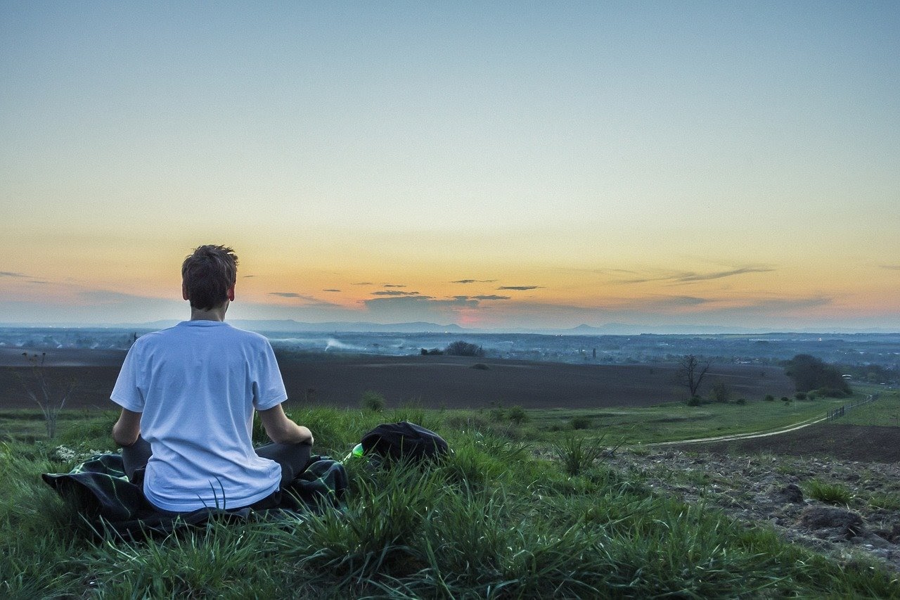 man meditates in field; teacher burnout concept