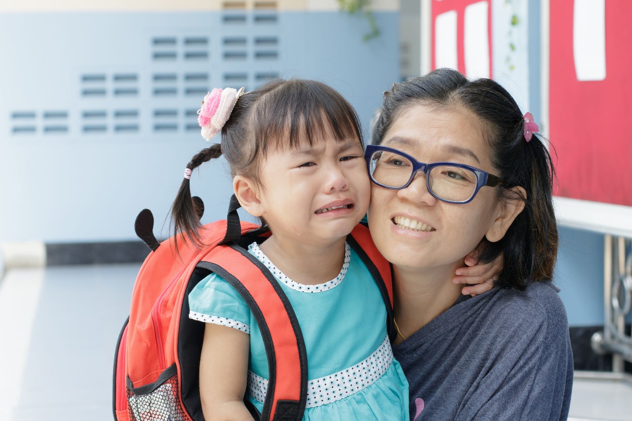 a crying child is comforted by her teacher; returning students concept