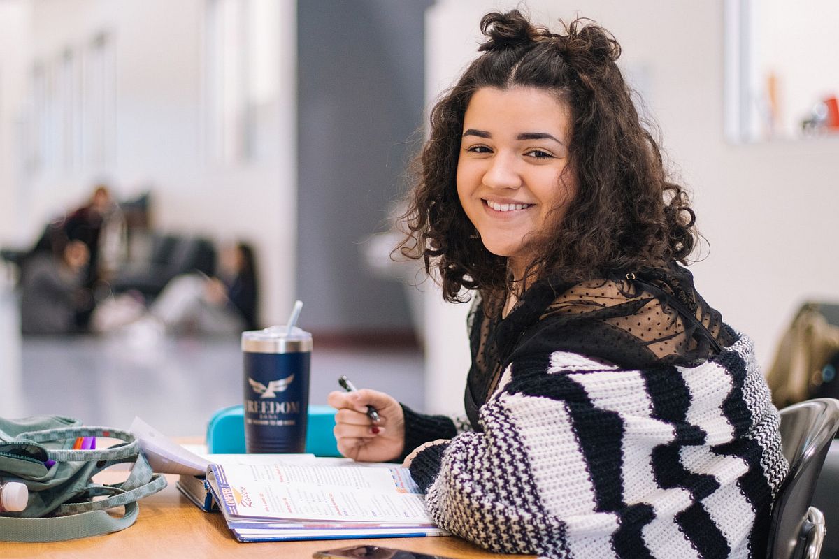 teenage student alone in study hall smiling at the camera; concept: classroom changes because of COVID