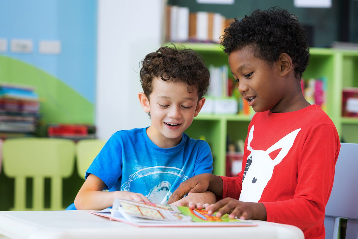 two kindergarteners share a book; remote learning and in-person learning concept