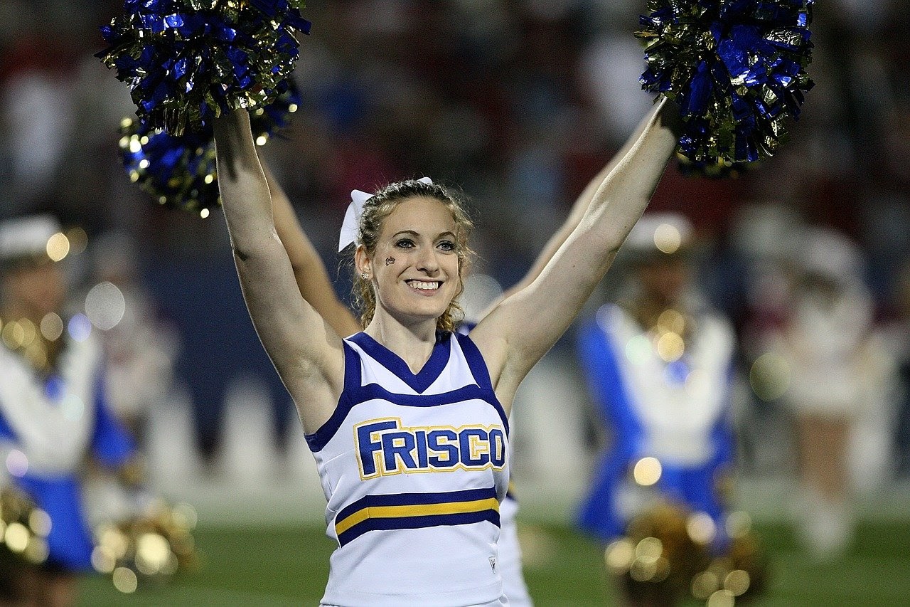 smiling cheerleader with arms raised holding pom-poms; concept: how counselors and educators can help juniors and seniors