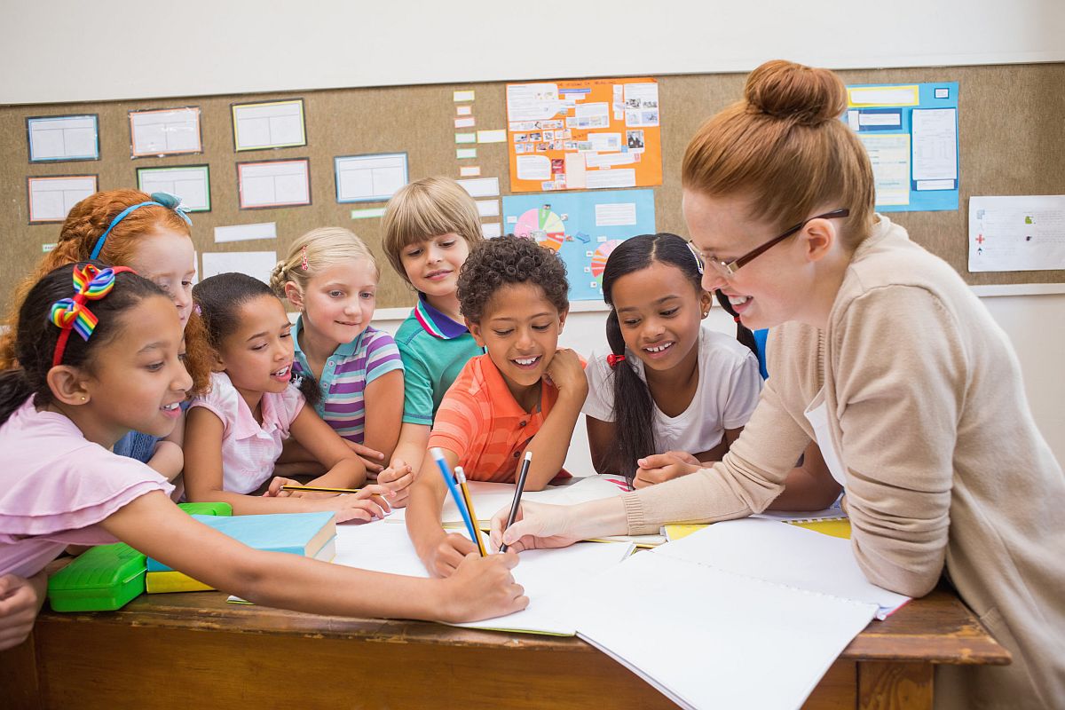 Teacher and pupils working at desk together at the elementary school, Columbus Day concept