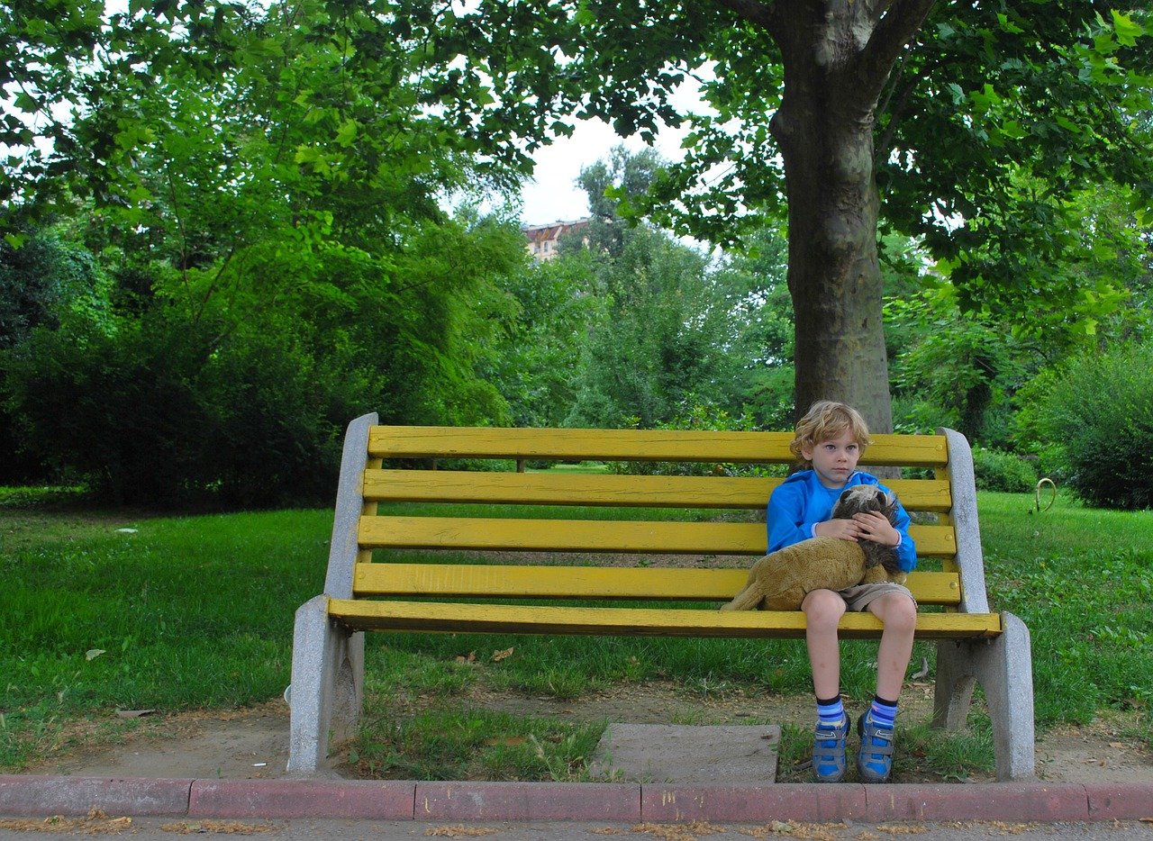 student clinging to a stuffed animal alone on a bench; side effects of remote learning concept
