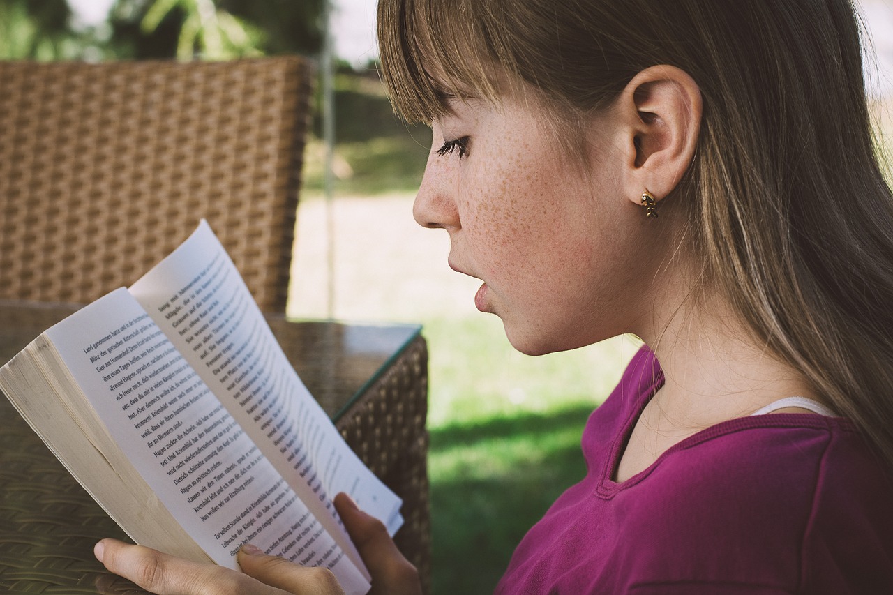 teenage girl with freckles and brown hair reading a book; book report lesson plans concept