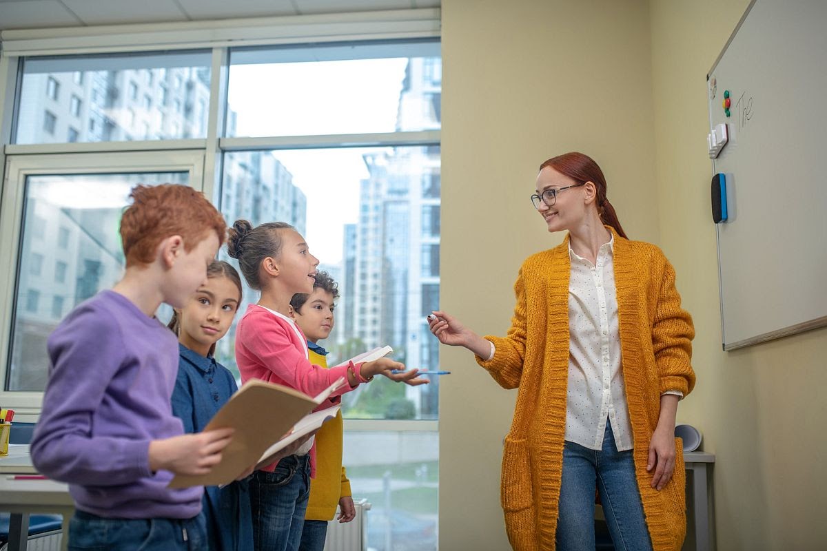 Teacher asking schoolchildren standing in front of whiteboard; teaching analytical reading concept