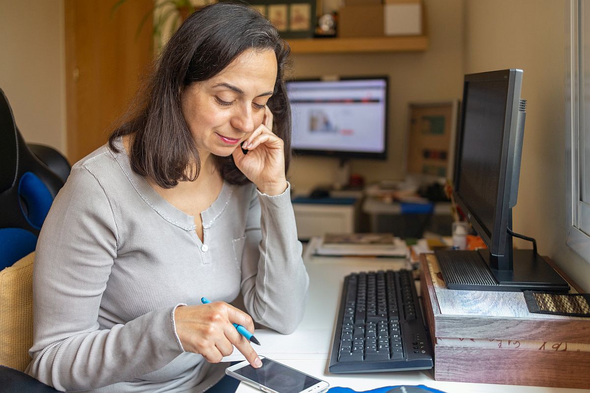 Middle aged woman online at home, sends a message on smartphone; making the most of planning period concept