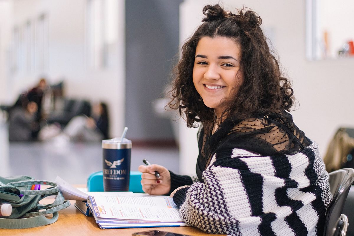 smiling student in black and white sweater looks at camera while working on homework; group work and social-emotional learning concept