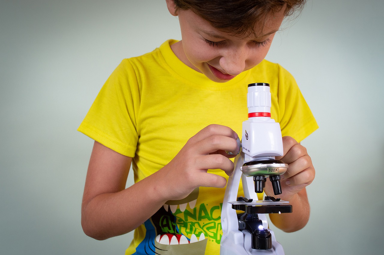 young male student looking through microscope; science podcasts for students concept