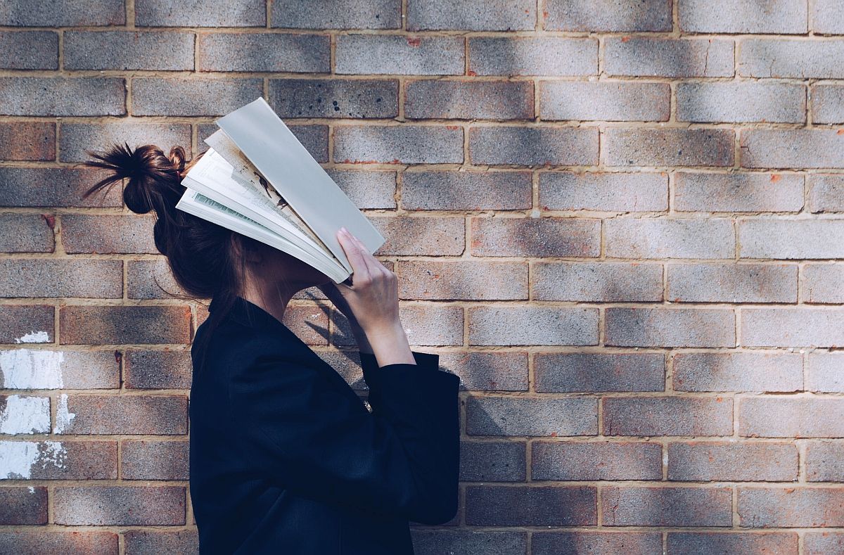 Girl outside putting an open book over her face; social emotional concept