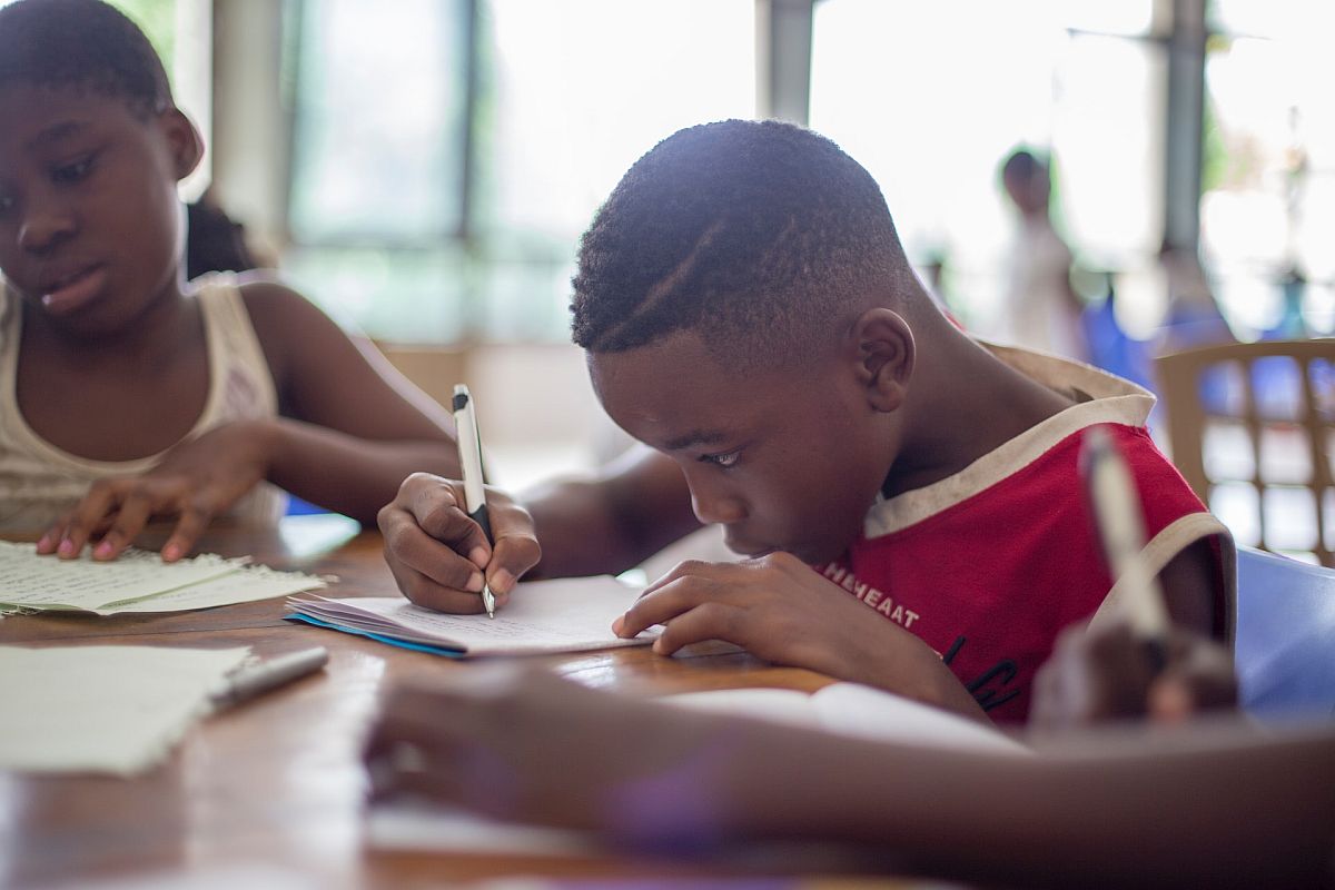 Students writing at classroom table; paraprofessionals in education concept.