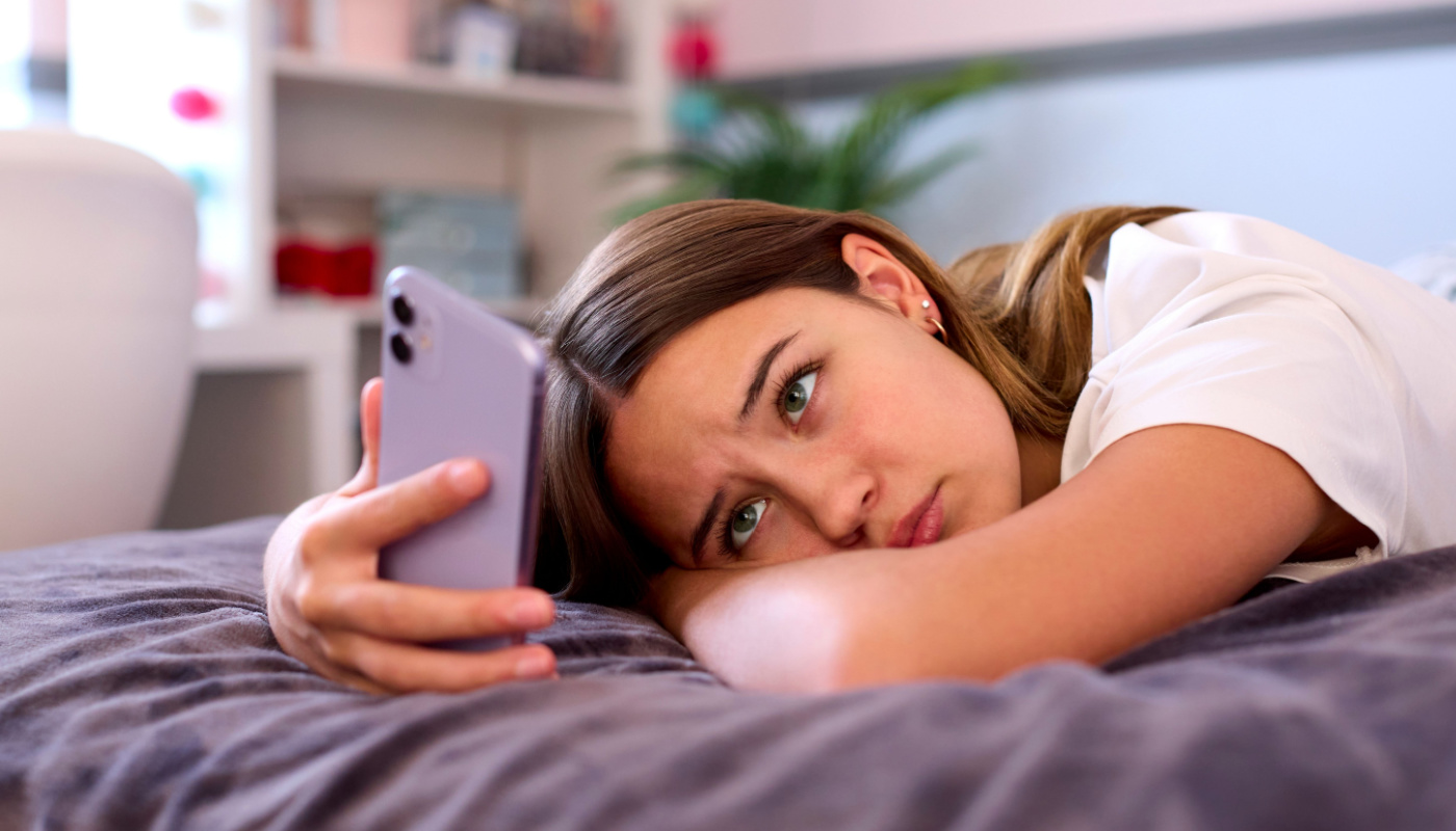 Concerned teenage girl looking at her phone; social media and body image concept 