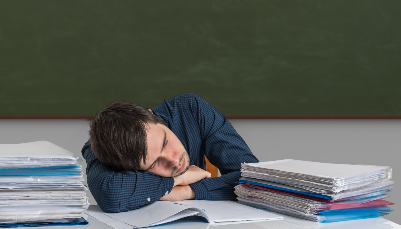 Teacher asleep at his desk; later school start times concept